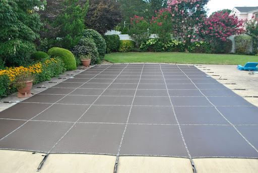 An in-ground pool is shown with a LOOP-LOC Aqua-Xtreme Mojave Brown cover. Orange flowers are shown in pots next to the pool.