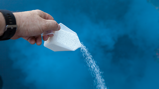 A man pours chlorine into a pool.